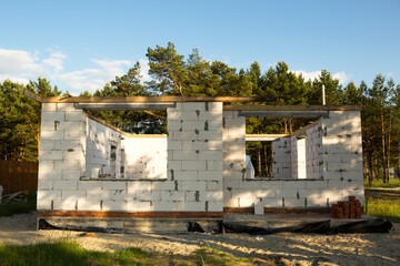 Fototapeta na wymiar The object of unfinished construction is a future house made of a porous concrete block. 1st floor with an attic. Housing in rural areas is under construction. Walls with windows