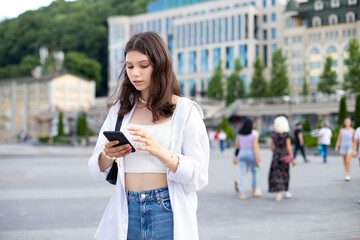 Fashionable teen girl in casual clothes uses phone while standing in the middle of the street. world tourism day