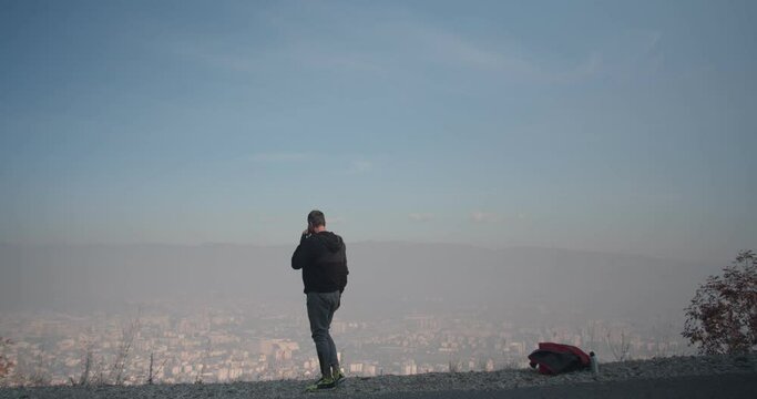 Olde man stretching his legs while talking on the phone and looking at a city