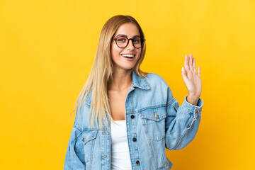 Young blonde woman isolated on yellow background saluting with hand with happy expression © luismolinero