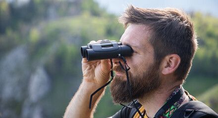 handsome man trekking in nature using binoculars slow travel