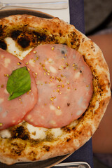 Close up. Traditional Italian round pizza with prosciutto and ham (mortadella), pistachio, basil and mozzarella cheese at the restaurant in Milan, Lombardy, Italy. European food and snacks. 