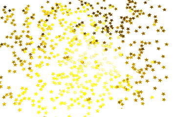 Gold sequins in the shape of stars shimmer on a white background. Backgrounds with copyspace for a...