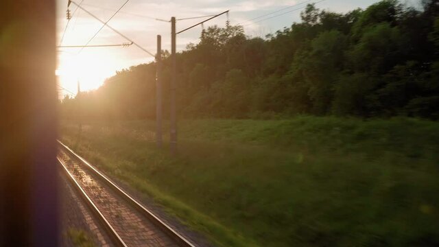 view from window high-speed train on landscape of beautiful nature wild field and forest railroad tracks rails on evening sunset in summer background. Transport, travel, railway, communication concept