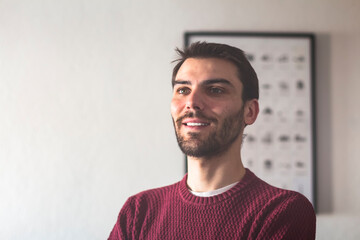 Obraz premium Portrait of a young adult caucasian man smiling and relaxing on a couch in a bright and white apartment 