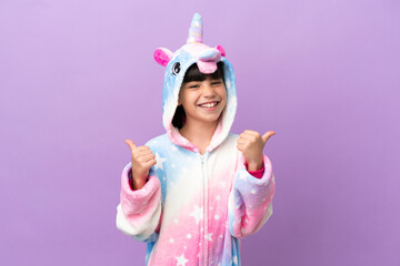 Little kid wearing a unicorn pajama isolated on purple background with thumbs up gesture and smiling