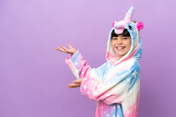 Little kid wearing a unicorn pajama isolated on purple background extending hands to the side for...