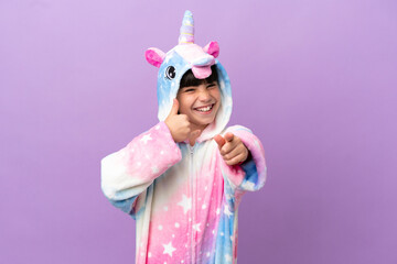 Little kid wearing a unicorn pajama isolated on purple background making phone gesture and pointing front