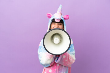 Little kid wearing a unicorn pajama isolated on purple background shouting through a megaphone
