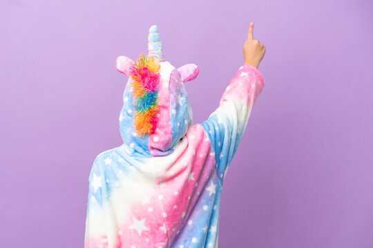 Little kid wearing a unicorn pajama isolated on purple background pointing back with the index finger