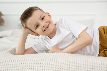 Obraz na płótnie Canvas Happy Child boy smiling and looking into the camera while lying on his side in bed. Kid Boy close-up on a white background, looking into the camera.