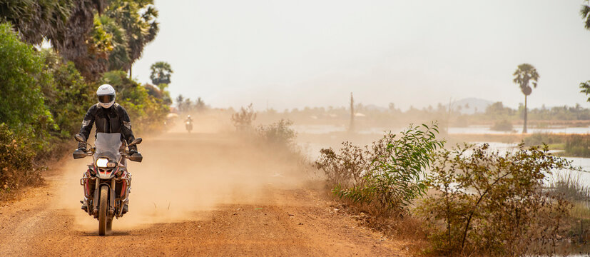 Man riding his adventure motorbike on dusty road in Cambodia