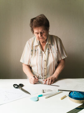 Elderly woman builds medical mask pattern on paper