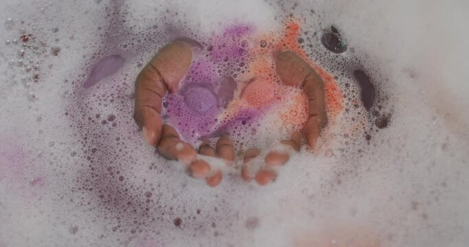 Hands of african american attractive woman taking bath with foam, salt and rose petals