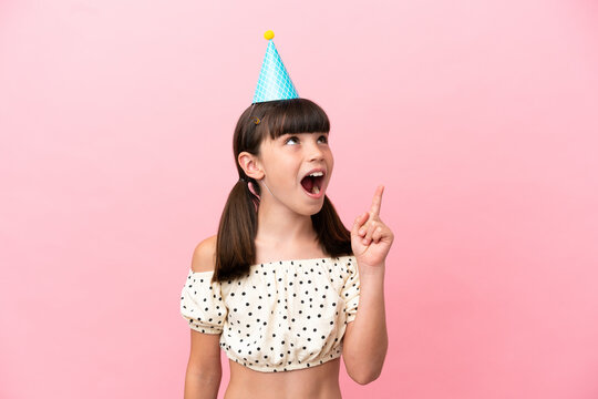 Little caucasian kid with birthday hat isolated on pink background thinking an idea pointing the finger up