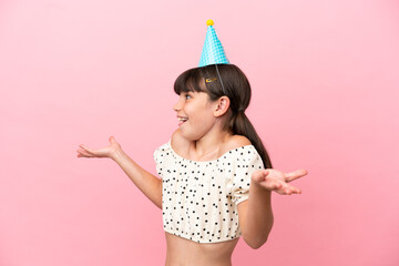Little caucasian kid with birthday hat isolated on pink background with surprise expression while...