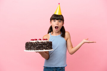 Little caucasian kid holding birthday cake isolated in pink background with shocked facial...