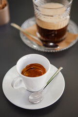 Traditional Italian coffee. The white espresso cup on a white saucer with a spoon and a crystal glass of  Americano coffee at the bar (coffeeshop) in Milan, Lombardy, Italy. European beverages.