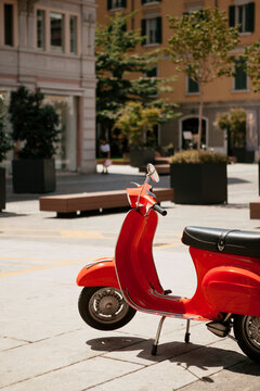 Close up. The Italian red scooter parked on a narrow Italian public street in the city center of Brescia, Lombardy, Italy. European traditional vehicle (motorcycle) outside on a sunny day.