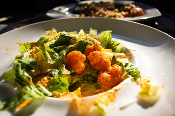 Green salad topped with fried shrimp and sauce