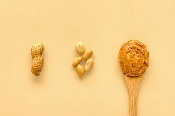 Peanuts and peanut butter in wooden bamboo spoon on beige background