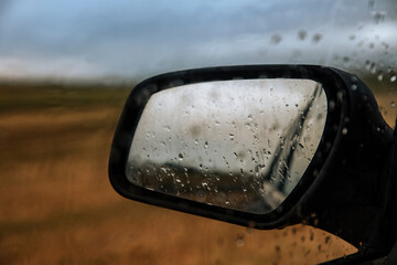 Raindrops reflecting on rear-view mirror of car in a field