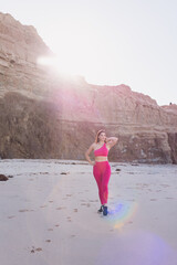 Woman wearing hot pink gym clothes exercising at the beach.
