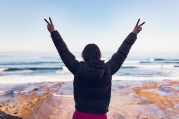 Woman wearing gym clothes looking at the ocean from the cliffs.