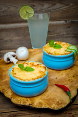 Pots with mushroom julienne on a wooden board, decorated with herbs. Julienne in cocotte with yellow cheese crust.