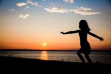 Silhouette of young girl dancing and twirling in the sunset