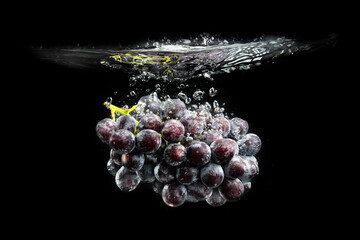 Isolated Red grapes splashing and sinking in water on black