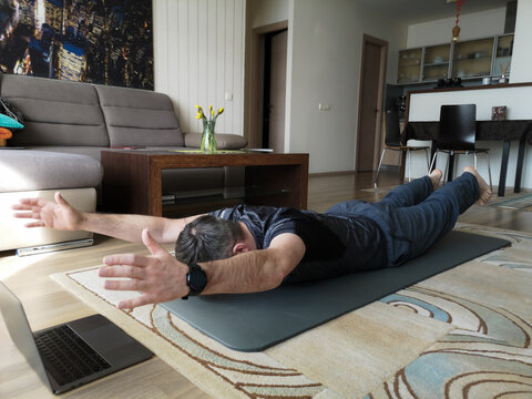 A man does yoga online at home on a gymnastics mat