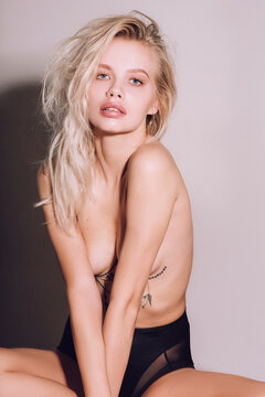 Closeup of pretty young woman face with blue eyes, blonde hair, has nude makeup, perfect soft skin, standing shirtless with bare shoulders, looking at camera. Studio grey background