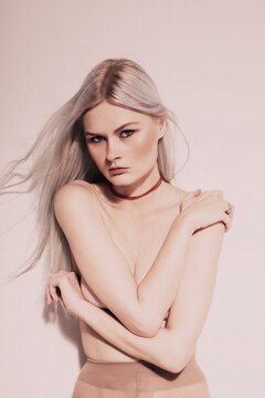 Studio Fashion Portrait Of Blonde Wearing red choker topless, hiding her chest
