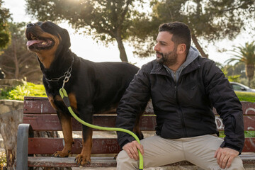 Man sitting on a park bench next to his rottweiler dog