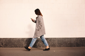 Side view of transgender woman using smart phone walking against wall