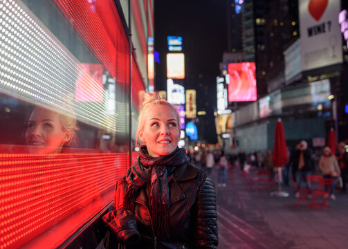 Cheerful woman standing near illuminated building wall in evening city