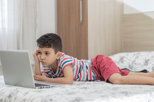Young boy child lying on bed using a laptop. Online class lesson