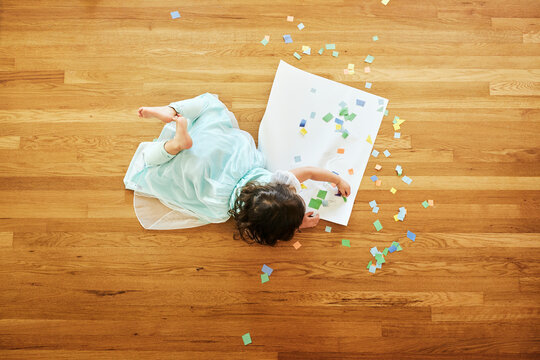 Girl doing craftwork with colorful papers while lying on hardwood floor at home