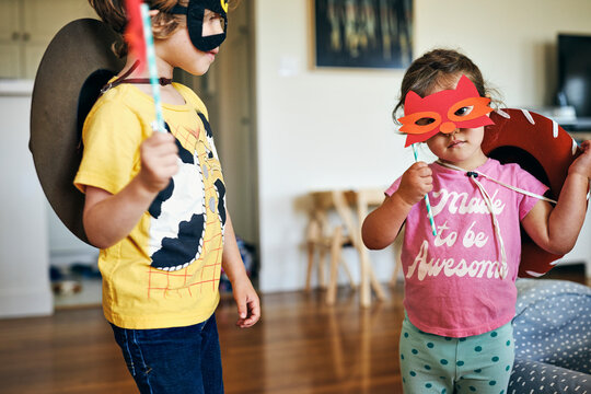 Brother and sister wearing masquerade masks at home