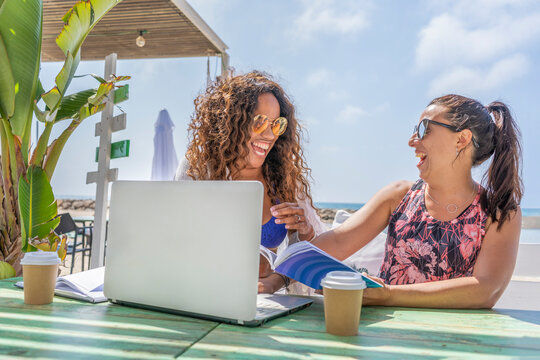 Happy business friends enjoy working together with laptop , drinking a coffee in amazing beach bar terrace.
