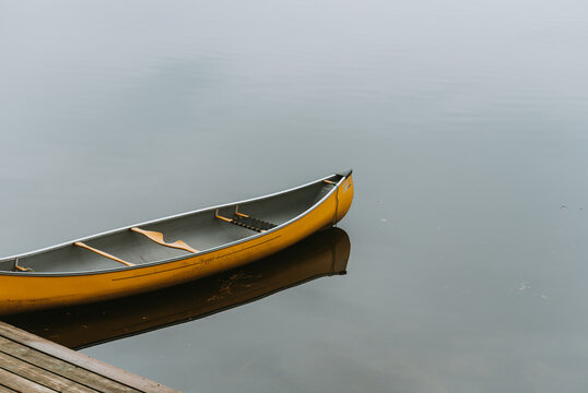 Empty yellow canoe at a wooden dock on a calm lake in Canada.