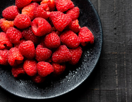 Close up of a bowl of fresh red raspberries on black background.