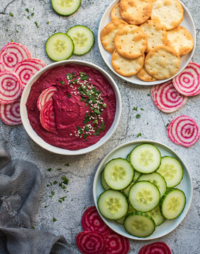 Bowl of beet hummus, vegetables and crackers on gray background.