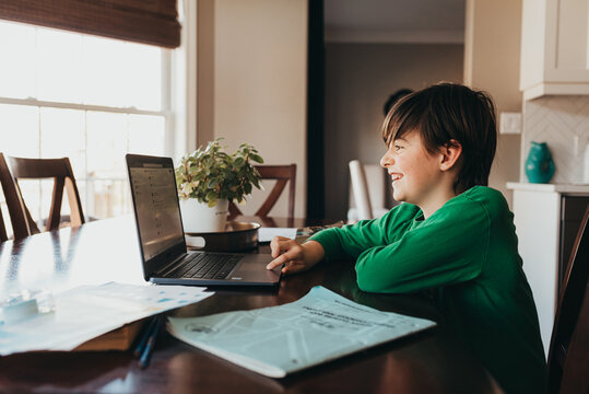 Happy boy doing on school work online on computer at kitchen table.
