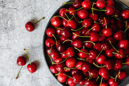 Large bowl of bright red cherries on a grey cement counter from above.