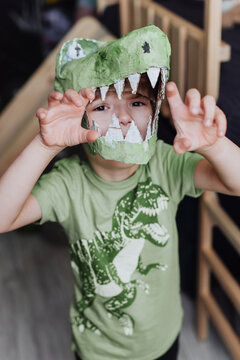 5 years boy playing in his room, wearing green t-shirt with dinosaurus print and t-rex mask