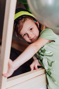 5 years boy playing in his room, wearing green t-shirt with dinosaurus print and dino helmet