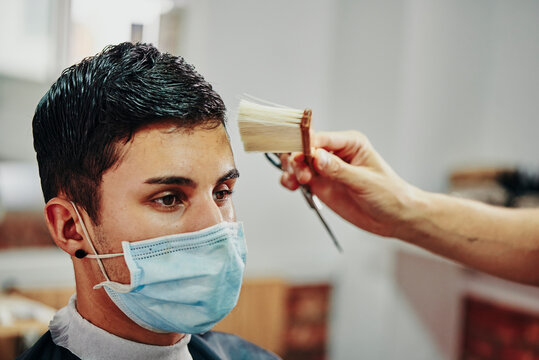 a boy with a face mask gets his hair brushed in the barber's shop