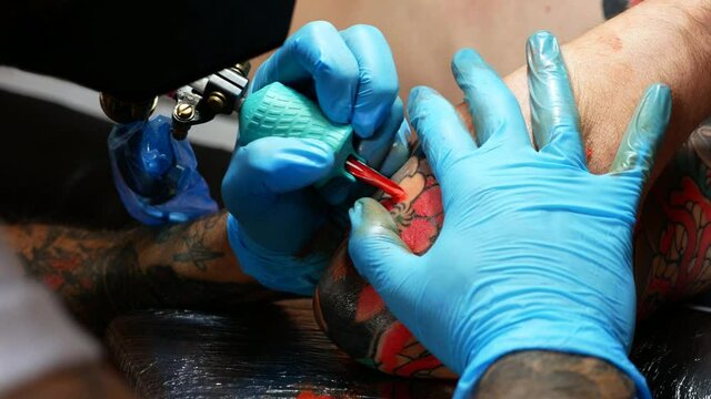 Close up of hands of an artist tattooing on a customer's arm.